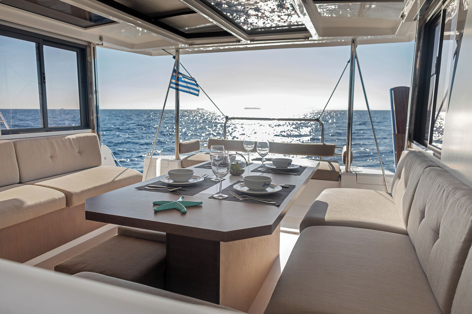 Un coin repas sur un bateau, avec une table dressée pour deux personnes, un drapeau et une vue sur la mer.