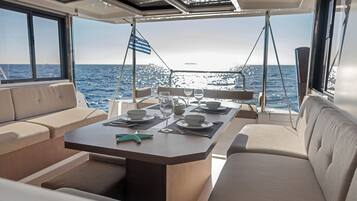 Un coin repas sur un bateau, avec une table dressée pour deux personnes, un drapeau et une vue sur la mer.