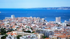 A coastal cityscape with dense urban buildings, a clear blue sea, and distant hills. - Sun-Kissed Sailing Adventure to Viejo Puerto (Marseilles)