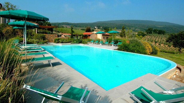 A swimming pool with lounge chairs and umbrellas, surrounded by greenery and hills. - Girasole in San Gimignano (San Gimignano)