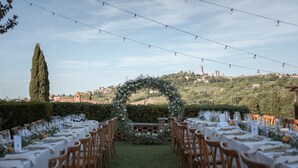 An outdoor wedding setup with tables, chairs, and a floral arch. - Girasole in San Gimignano (San Gimignano)