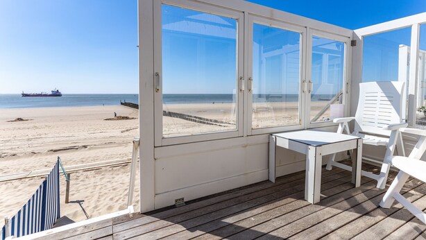Una terraza frente al mar con una mesa y sillas, vista a la playa y al océano, y un barco a lo lejos.