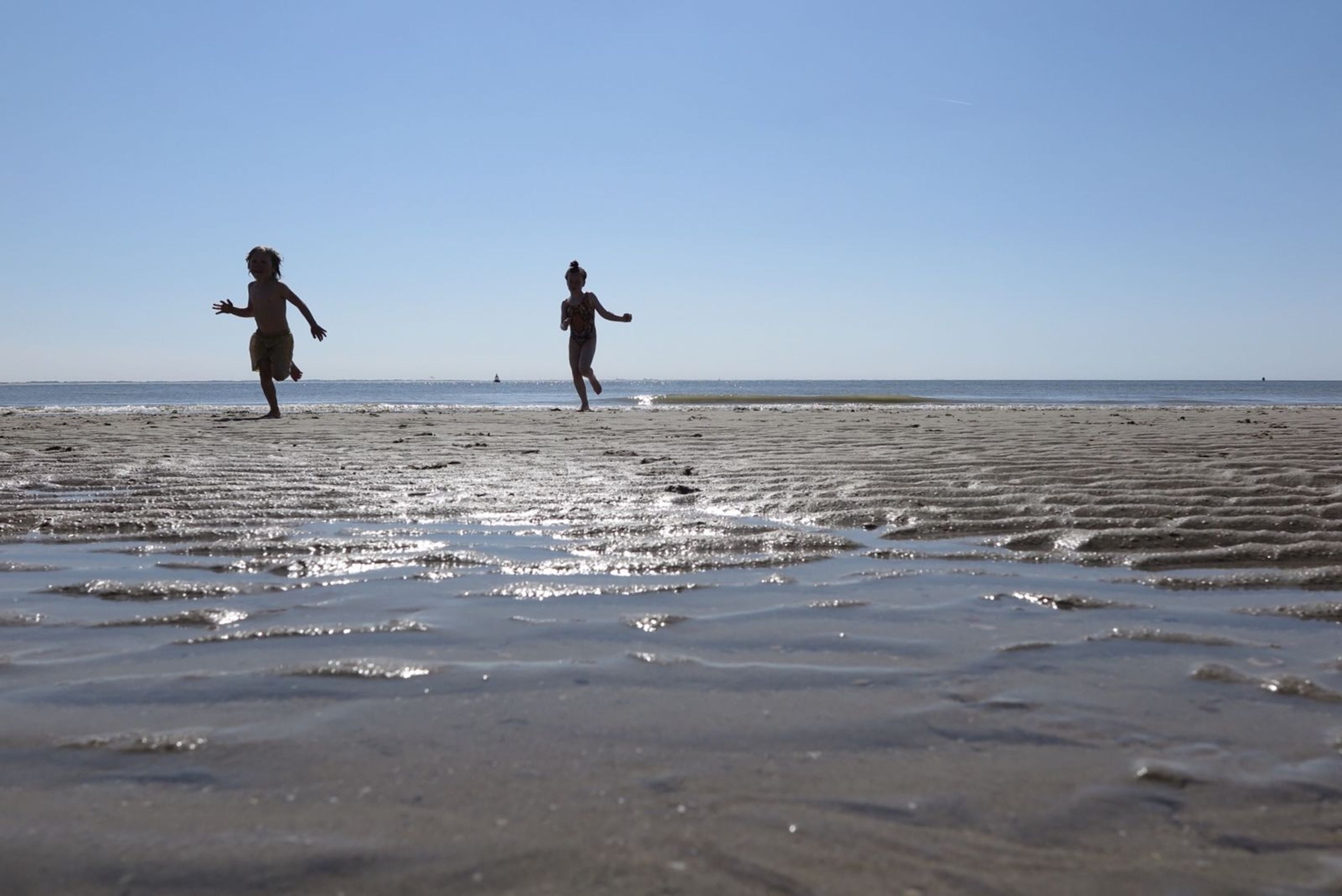 A beach with two people running.