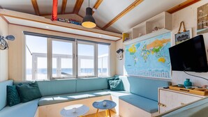 Una habitación acogedora con un ventanal grande, un sofá, dos mesitas y un mapa del mundo en la pared.
