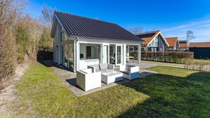 Ein modernes Haus mit überdachter Terrasse, Rasenfläche und blauem Himmel.