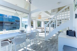 A modern interior with a dining area, white furniture, and a staircase leading to an upper level. - Zonnedorp 4 Villa Jula Renesse Comfortable Beach Villa for 6 People (Renesse)