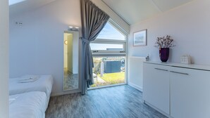 Ein Schlafzimmer mit einem Oberlicht, einem großen Fenster mit Vorhängen, einem weißen Kleiderschrank und einem kleinen Tisch mit einer Vase.