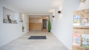 A hallway with a wooden floor, a black doormat, a plant, and a wooden cabinet with books. - Appartement - Winterbergerstrasse 3 Saphir Neuastenberg (Winterberg)