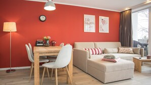 A modern living room with a red wall, a sofa, a dining table with chairs, and a lamp. - Appartement - Winterbergerstrasse 3 Saphir Neuastenberg (Winterberg)