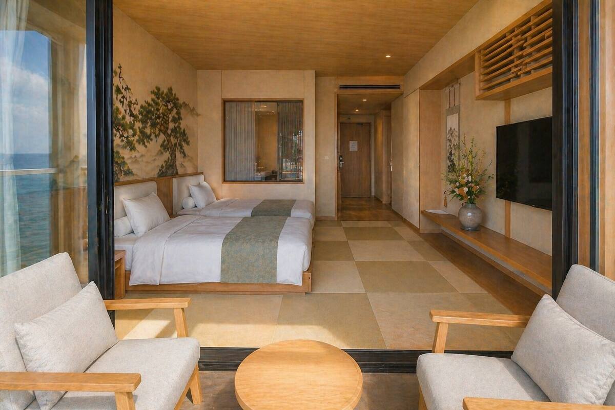 A modern hotel room with a large bed, two sofas, a TV, and a view of the sea.