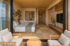 A modern hotel room with a large bed, two sofas, a TV, and a view of the sea.