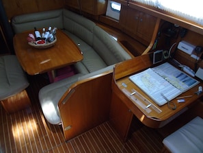 A compact boat interior with a dining area, a cushioned seating area, and a work desk with a map and navigation tools. - Sun-Kissed Sailing Adventure in the Ionian Islands, Lefkada (Lefkada)