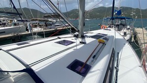 Un velero amarrado en un puerto deportivo, con vistas al mar y colinas al fondo.