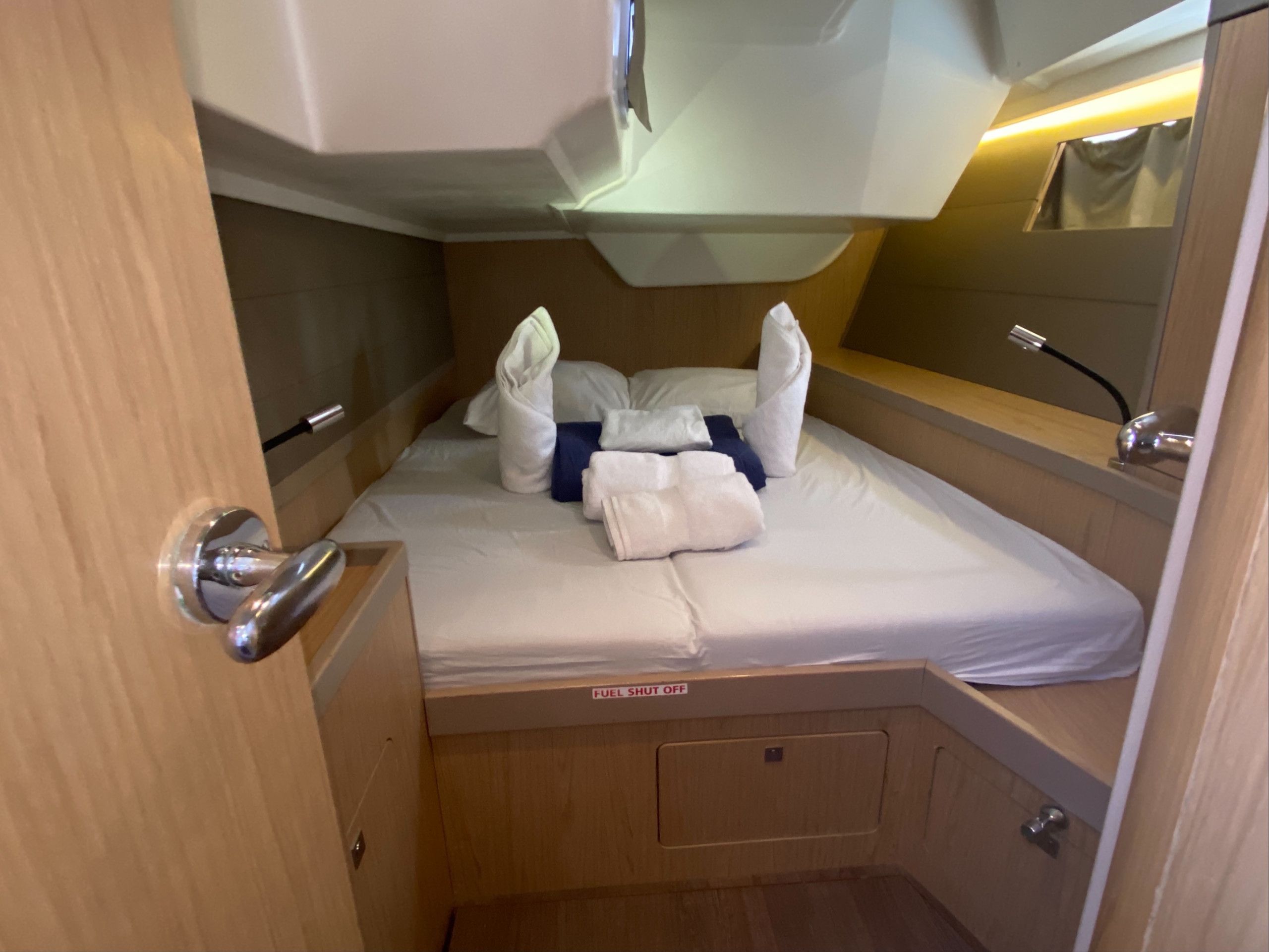Een compacte, goed verlichte hut met een bed, een 'FUEL SHUT OFF' bord, een spiegel en een klein houten kastje.