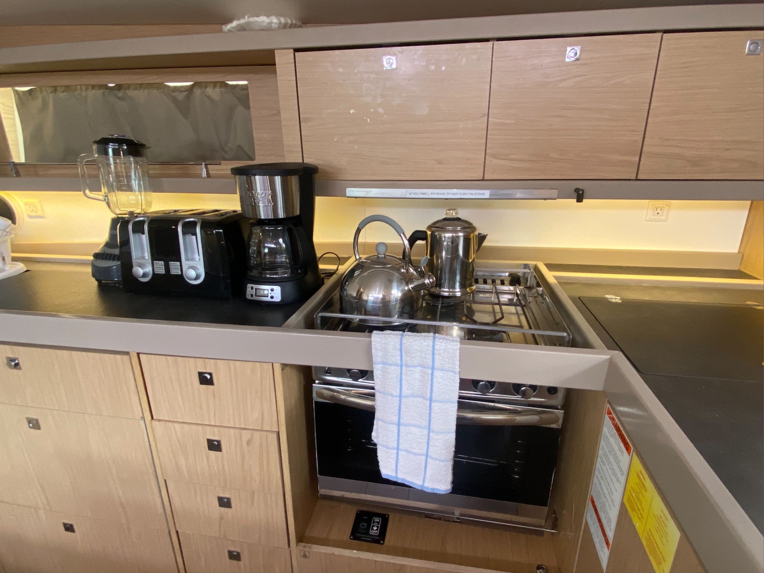 A compact kitchen with a coffee maker, kettle, toaster, and a stove.