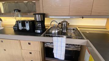 A compact kitchen with a coffee maker, kettle, toaster, and a stove.