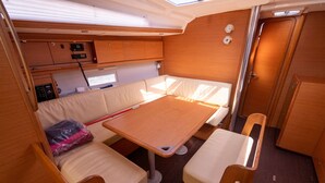 A compact interior with a table, two chairs, a cushioned bench, a control panel, and a door. - Sun-Kissed Sailing Adventure in Provence-Alpes-Côte d'Azur (Saint-Mandrier-sur-Mer)