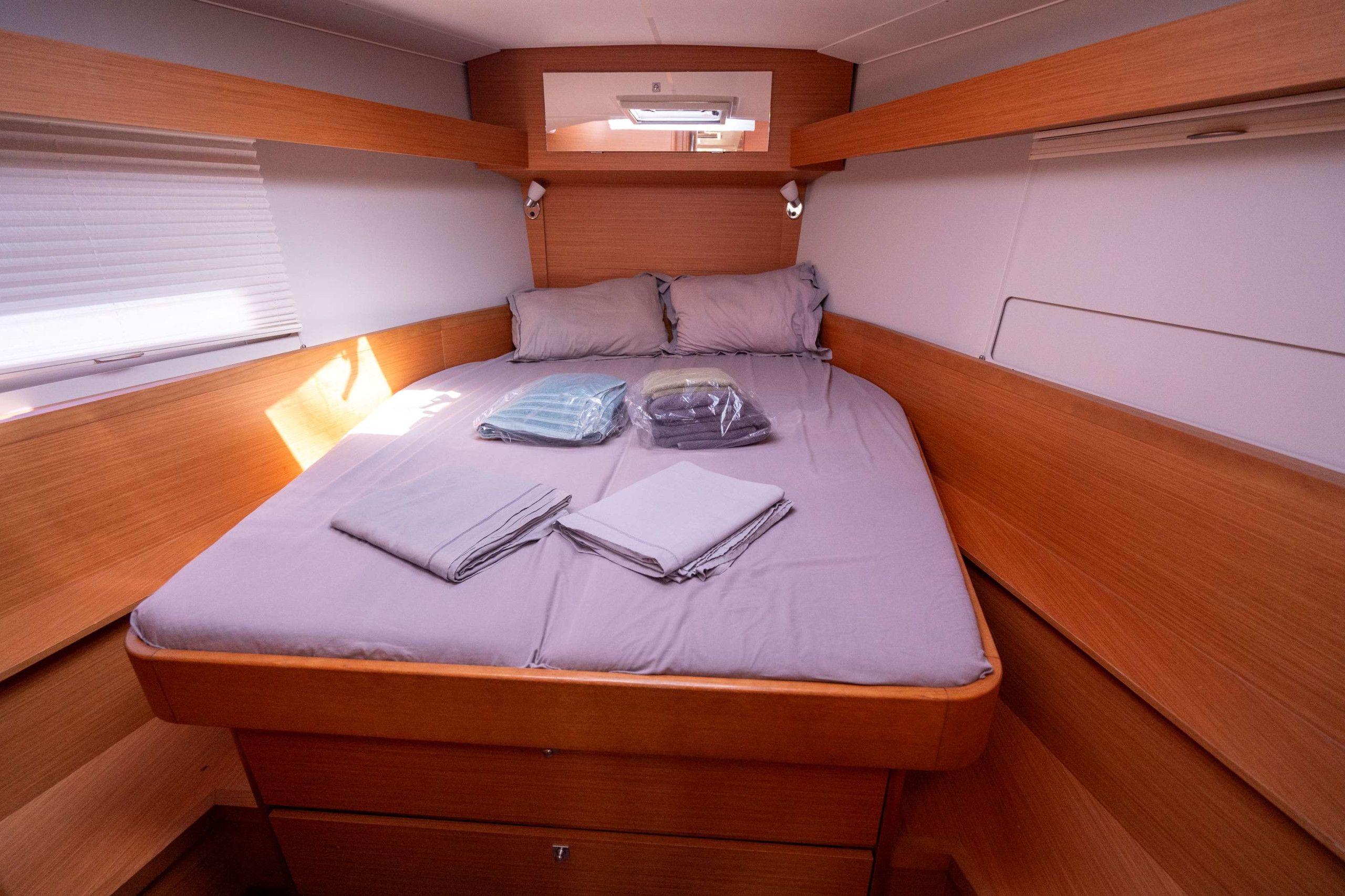 A compact, single-bed cabin with a wooden headboard, a window with blinds, and a small overhead light.