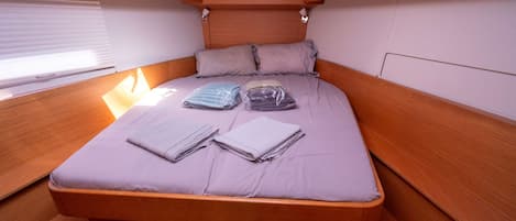 A compact, single-bed cabin with a wooden headboard, a window with blinds, and a small overhead light.