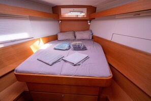A compact, well-lit cabin with a single bed, wooden headboard, and a small window.