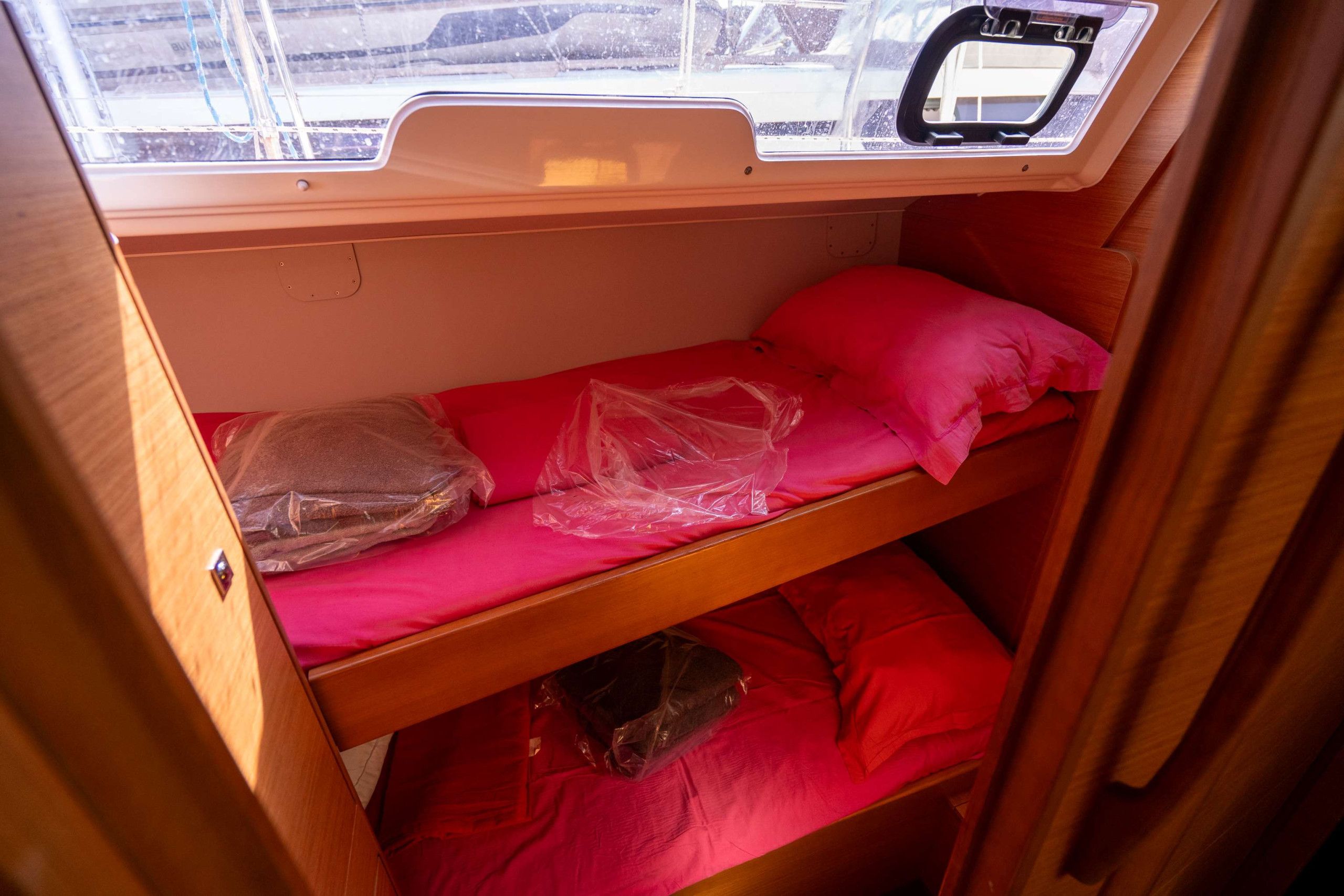 Una cama litera compacta con ventana encima, paredes de madera y colchón rojo.