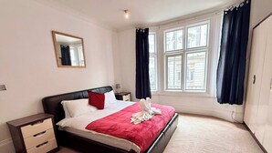 A hotel room with a large bed, a nightstand, a mirror, and a window with curtains. - Stylish 2BR Apt | Walk to New Street & Colmore Row (Birmingham)