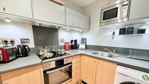 A modern kitchen with stainless steel appliances, wooden cabinets, a built-in oven, a dishwasher, and a microwave above the sink. - Stylish 2BR Apt | Walk to New Street & Colmore Row (Birmingham)