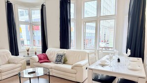 A modern living room with a white sofa, a glass coffee table, and a dining table set for two. - Stylish 2BR Apt | Walk to New Street & Colmore Row (Birmingham)