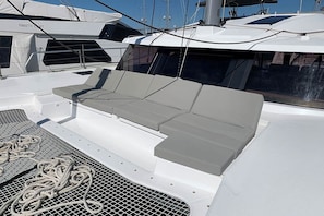 A yacht's deck with a grey cushioned seating area, a white railing, and a netted section. - Caribbean Dream: Sun-soaked Sailing Adventure from Tortola, Islas Vírgenes Británicas (Road Town)