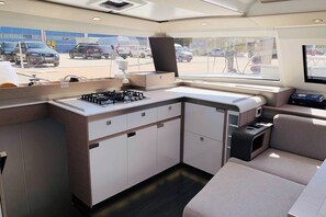 A compact kitchen with a gas stove, cabinets, and a seating area. - Caribbean Dream: Sun-soaked Sailing Adventure from Tortola, Islas Vírgenes Británicas (Road Town)