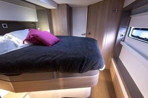 A bed with a dark cover and a single pink pillow, a wooden headboard, and a white wall with a window.