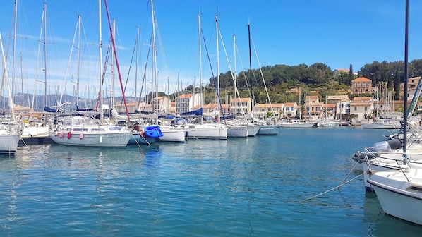 A marina with multiple sailboats docked, surrounded by buildings with red-tiled roofs.