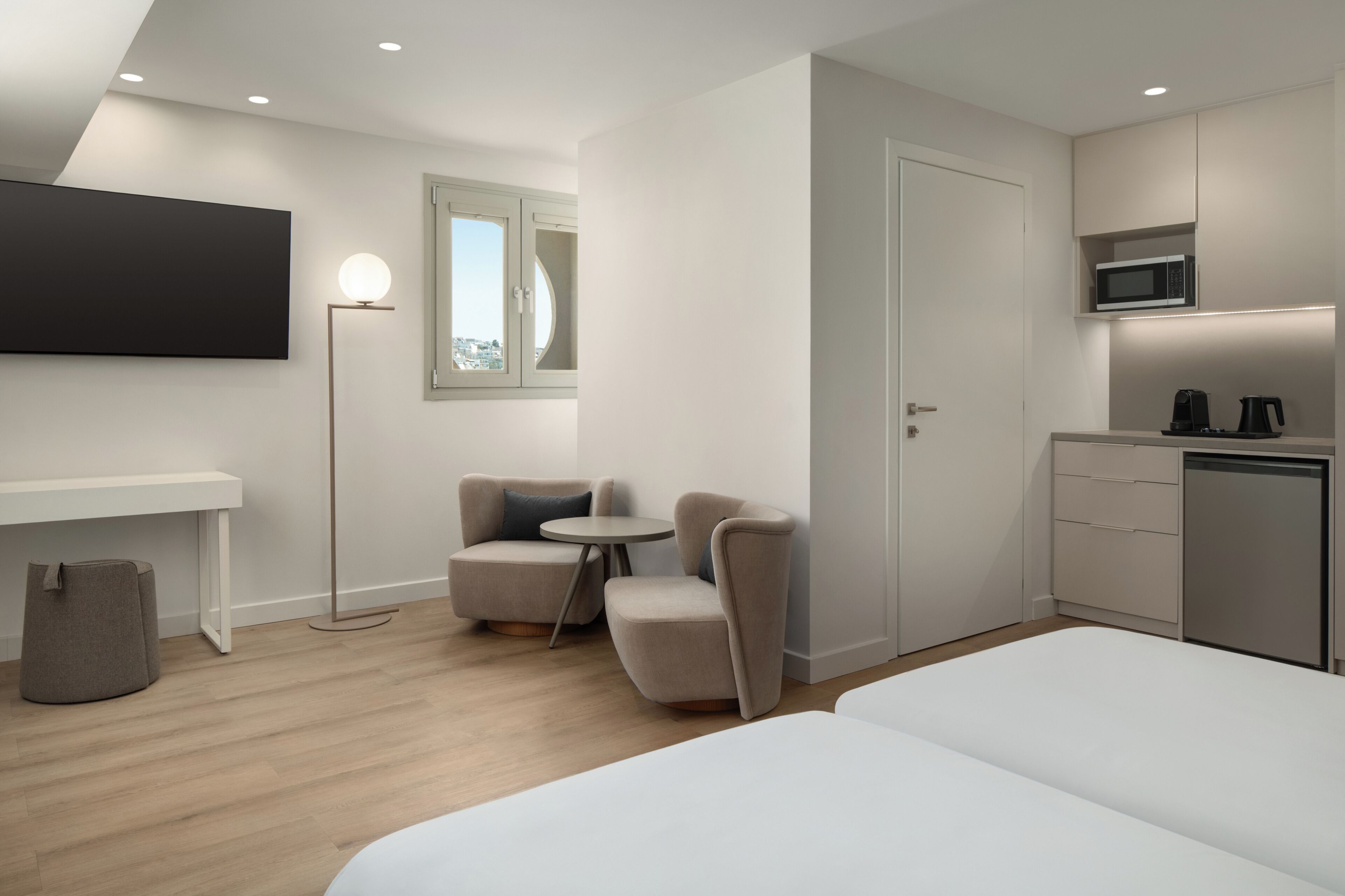 A modern hotel room with a bed, a desk, a chair, a small table, a microwave, and a coffee maker.