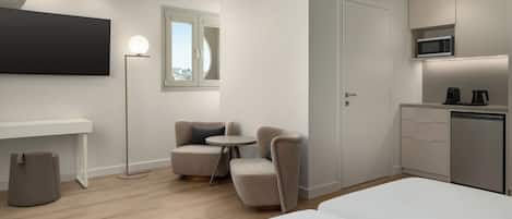 A modern hotel room with a bed, a desk, a chair, a small table, a microwave, and a coffee maker.