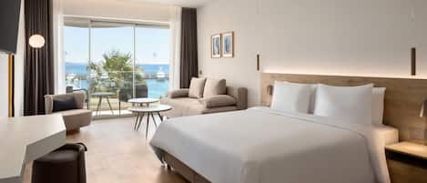 Une chambre d’hôtel moderne dotée d’un grand lit, d’un bureau et d’un balcon offrant une vue sur la mer.