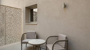 Un pequeño espacio al aire libre con dos sillas y una mesa, un muro decorativo con motivos de hojas y una ventana con vistas.