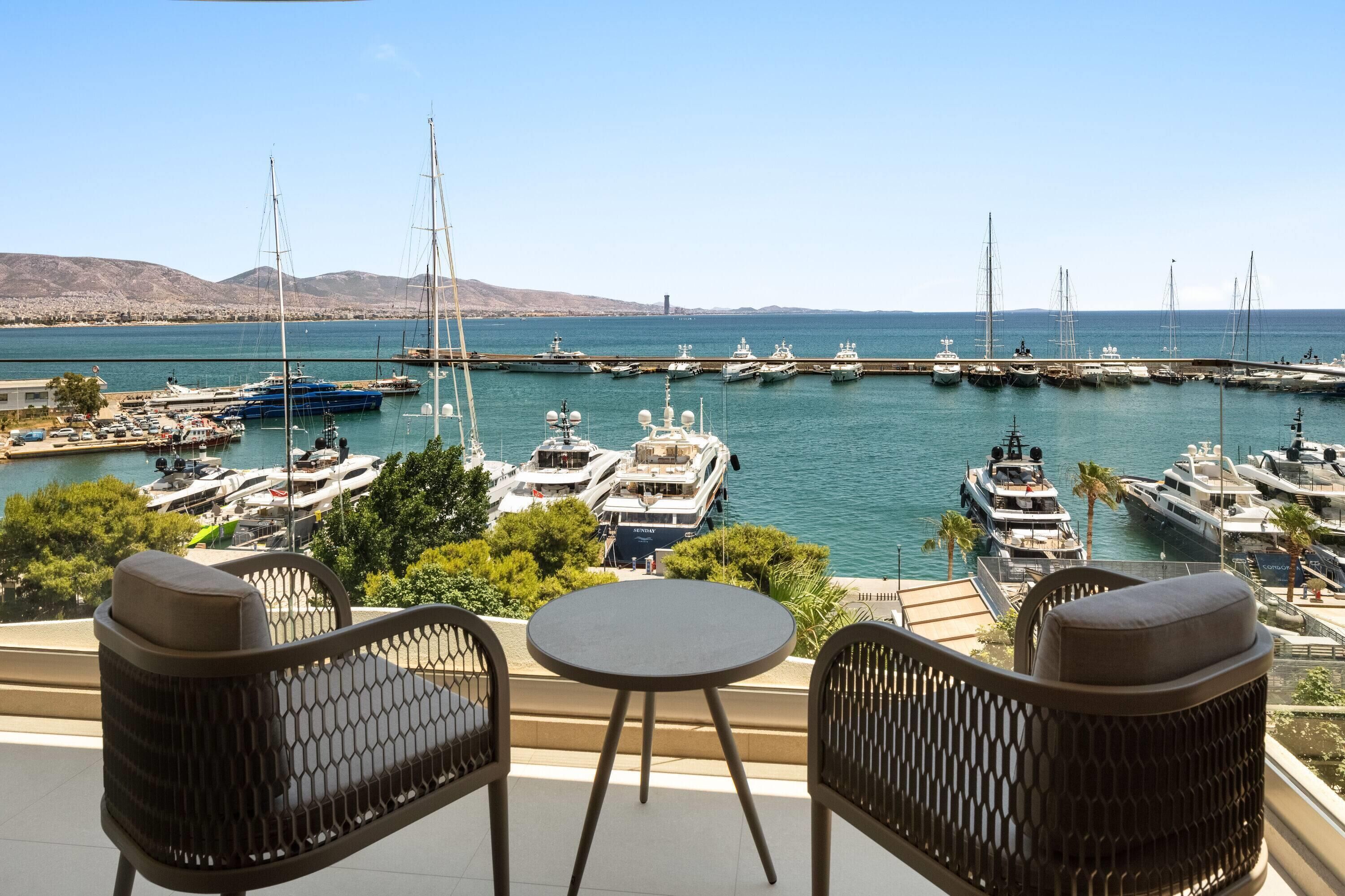 Puerto deportivo con varios yates amarrados, vista del mar y una mesa con sillas al frente.