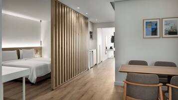 Una habitación de hotel moderna con cama, escritorio, una mesa de comedor con sillas, una cocina y una sala de estar con televisor.