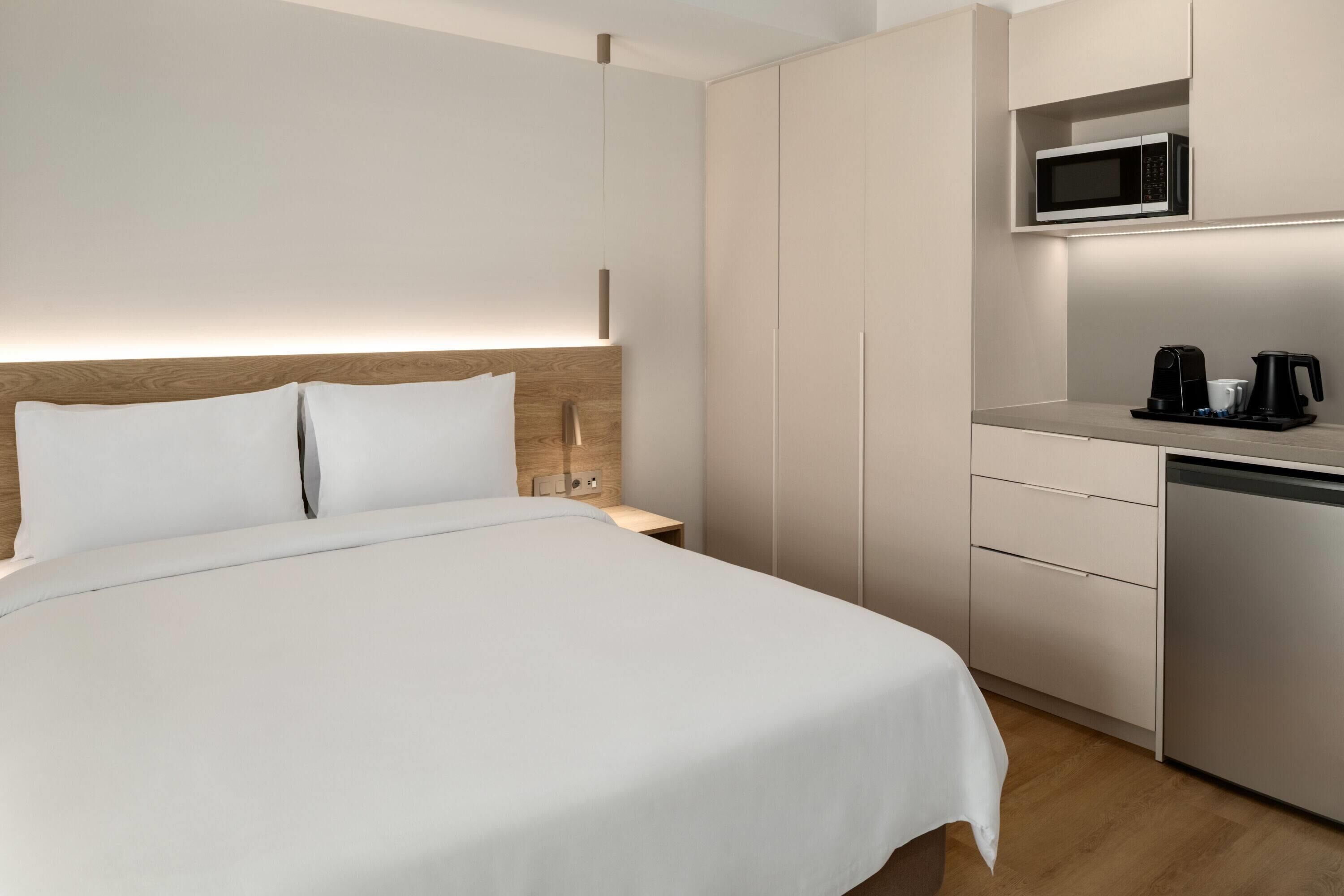 A hotel room with a bed, bedside table, a microwave, and a coffee maker.