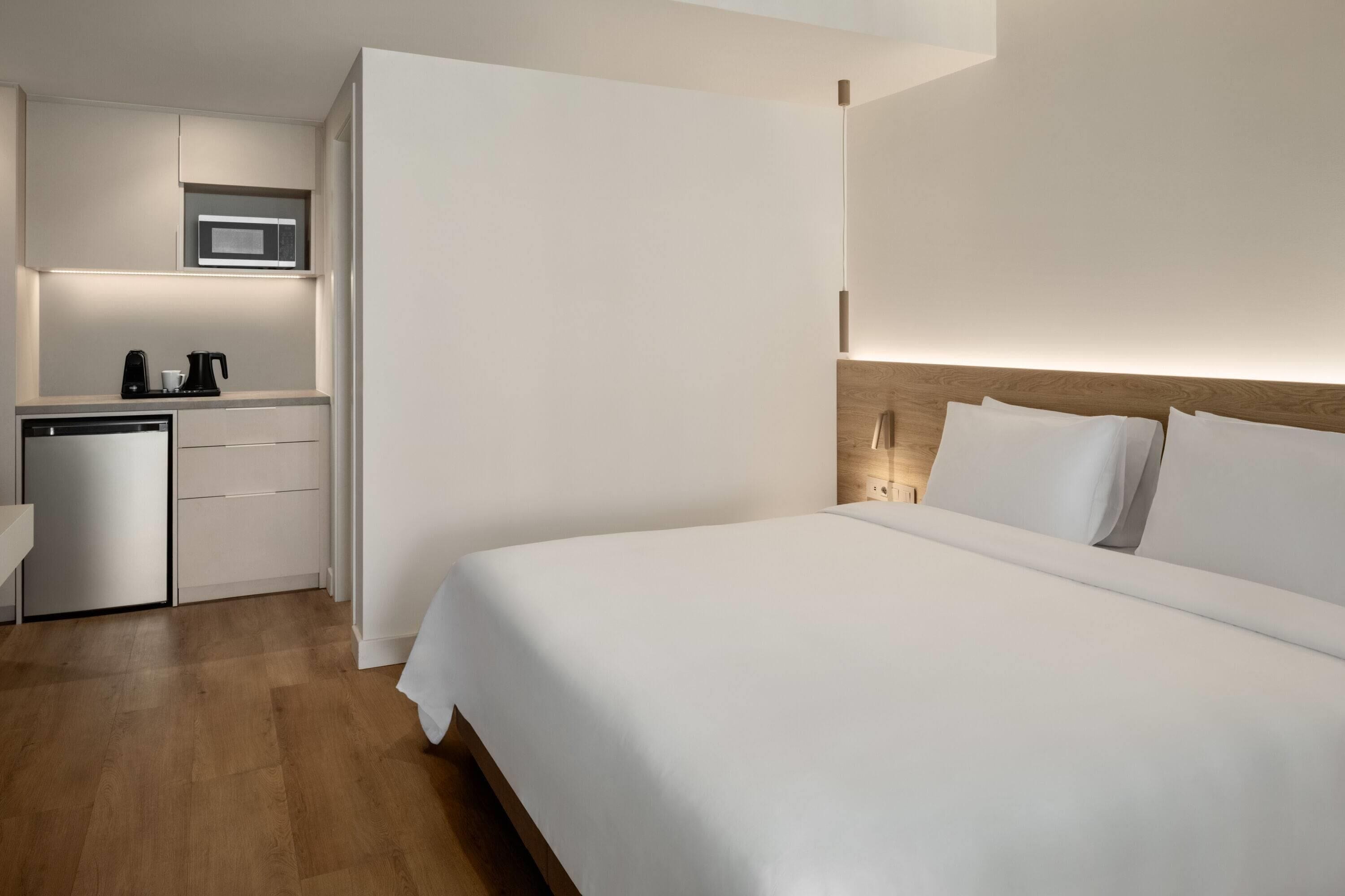 A hotel room with a bed, a small kitchenette with a microwave, and a wooden floor.