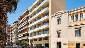 Un edificio residencial de varios pisos con balcones, un estacionamiento y una palmera.