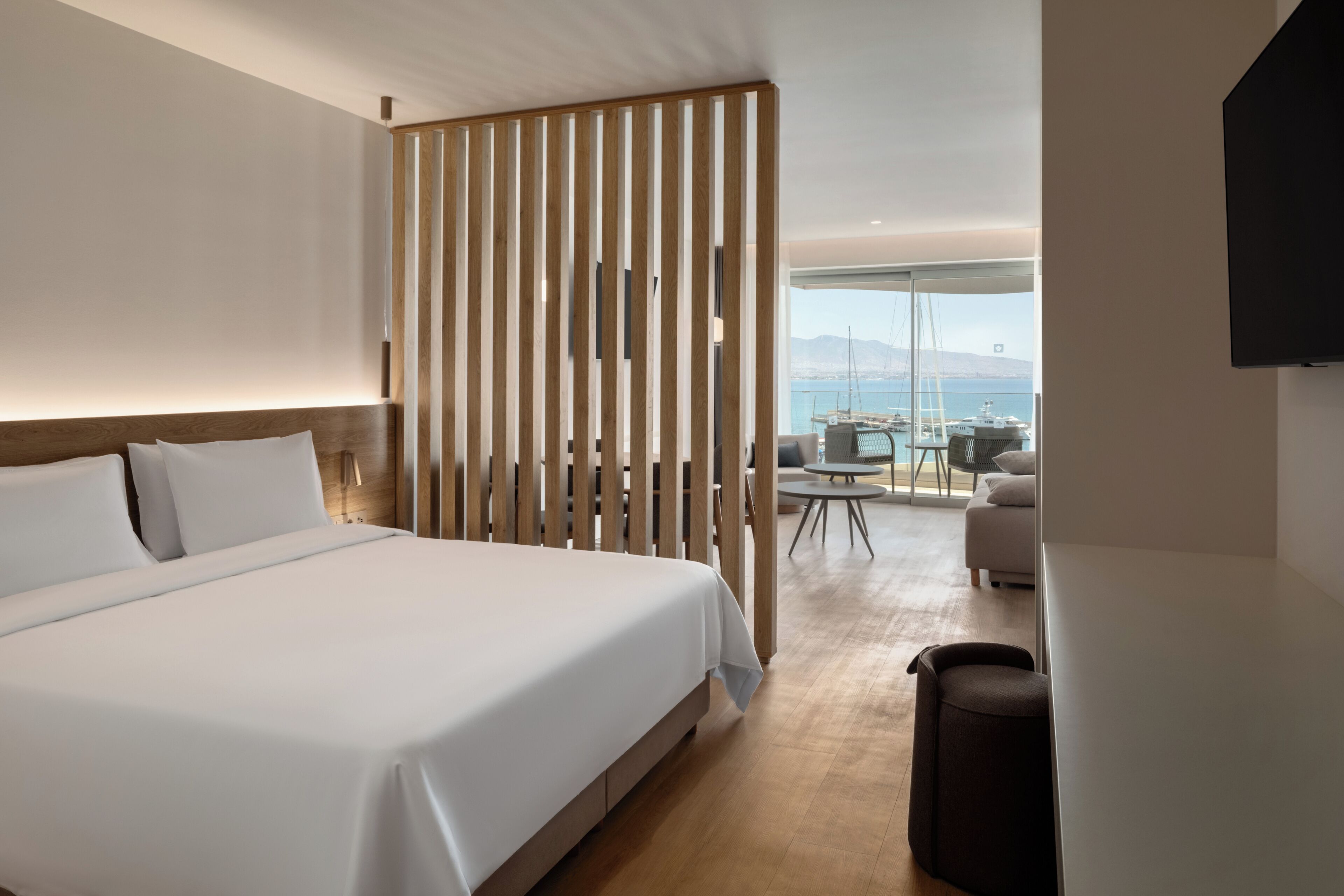 Une chambre d’hôtel dotée d’un grand lit, d’une cloison en bois, d’un coin salon avec une table et des chaises, et offrant une vue sur la mer.
