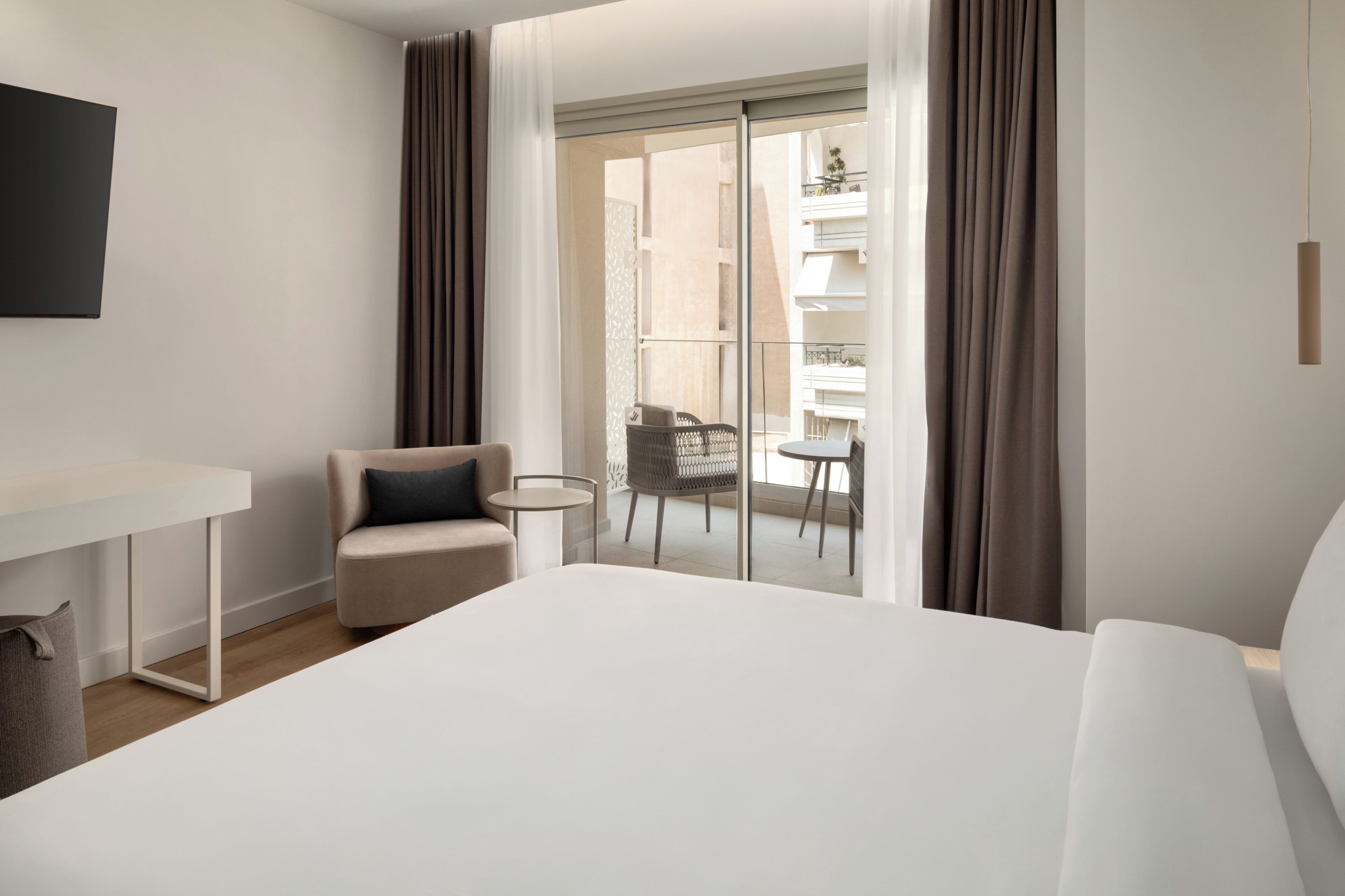 A hotel room with a bed, a desk, a chair, and a balcony with a table and chairs.