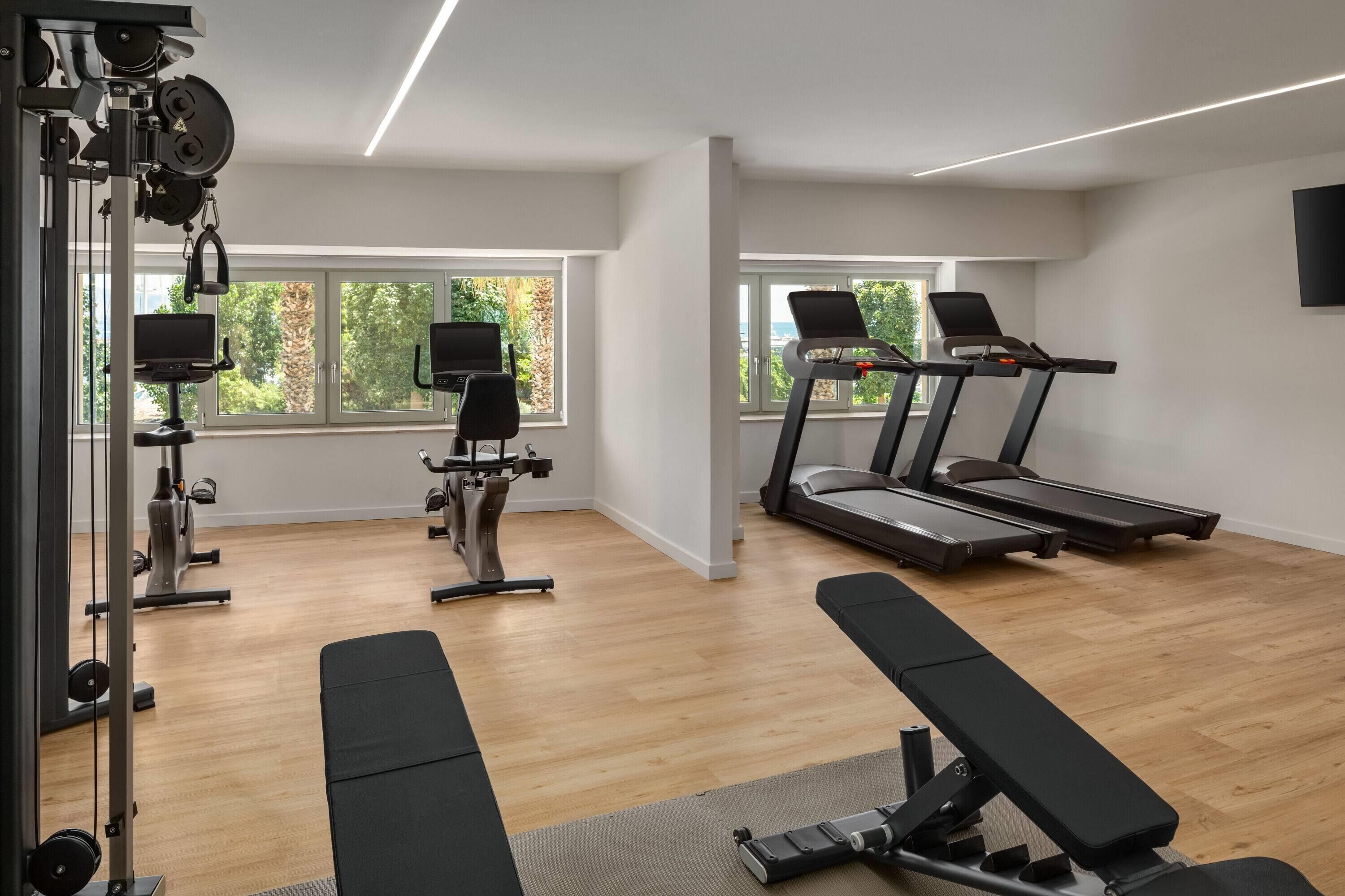 A modern gym with cardio equipment, weight machines, and a bench.