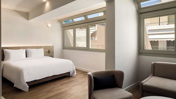 Habitación de hotel con cama, dos sillones, una mesita y ventana con vistas al exterior.