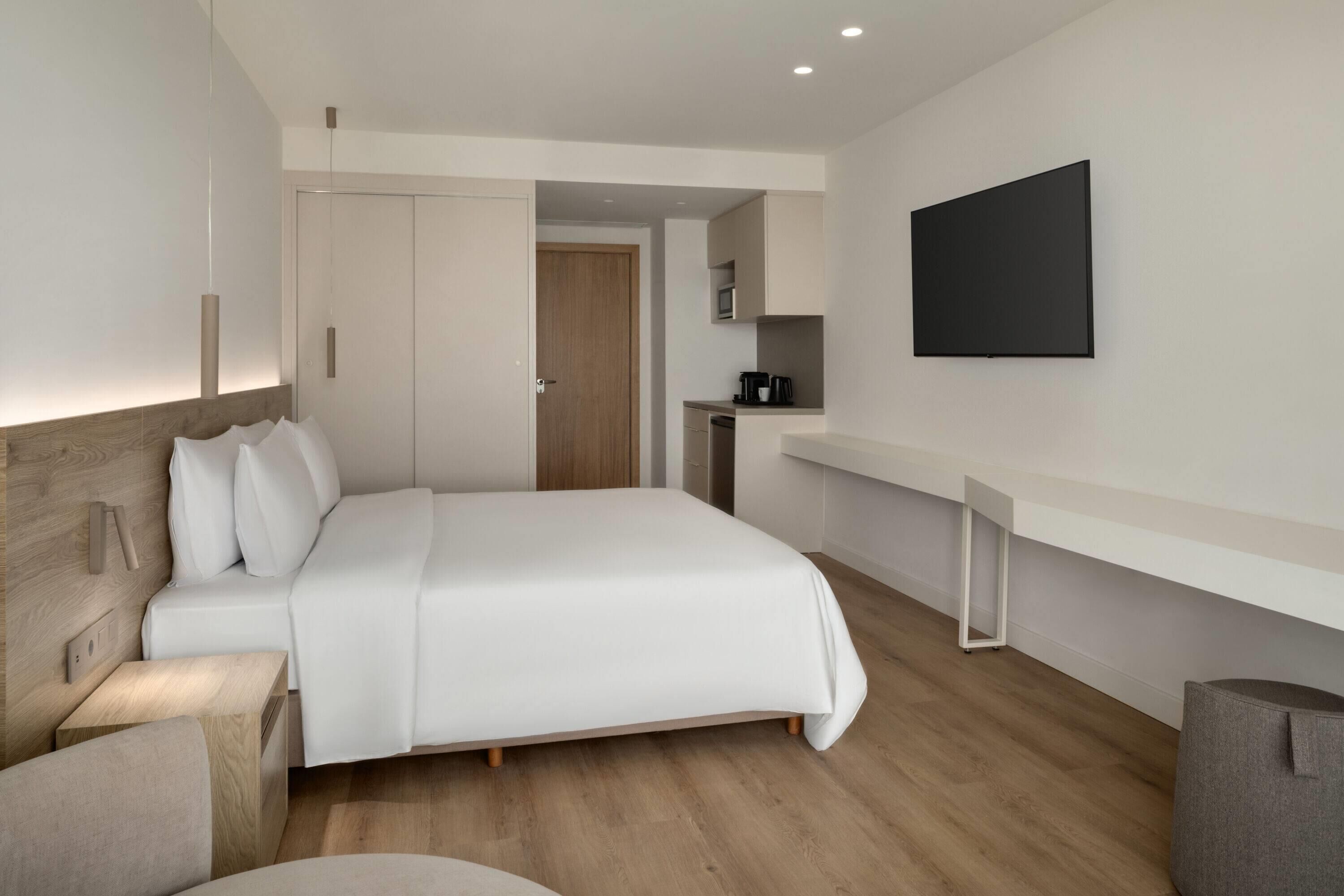A modern hotel room with a large bed, a desk, a coffee machine, and a flat-screen TV.