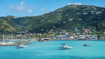A coastal marina with multiple sailboats docked, surrounded by a hilly landscape with buildings.
