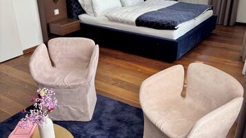 A hotel room with a bed, two armchairs, a small round table with a vase of flowers, and a painting on the wall.