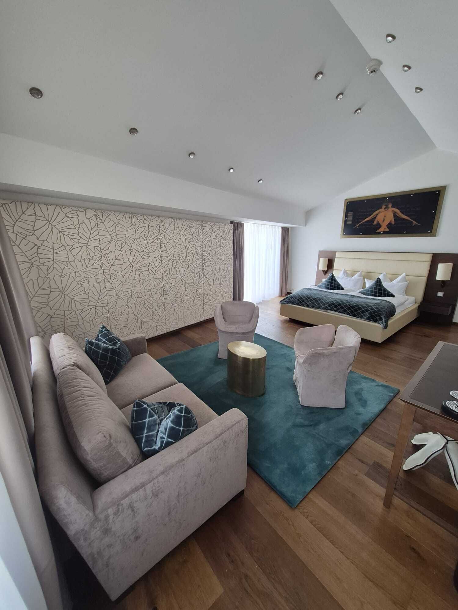 Et moderne hotelværelse med sofa, lænestol, rundt sofabord og seng med sengegavl.