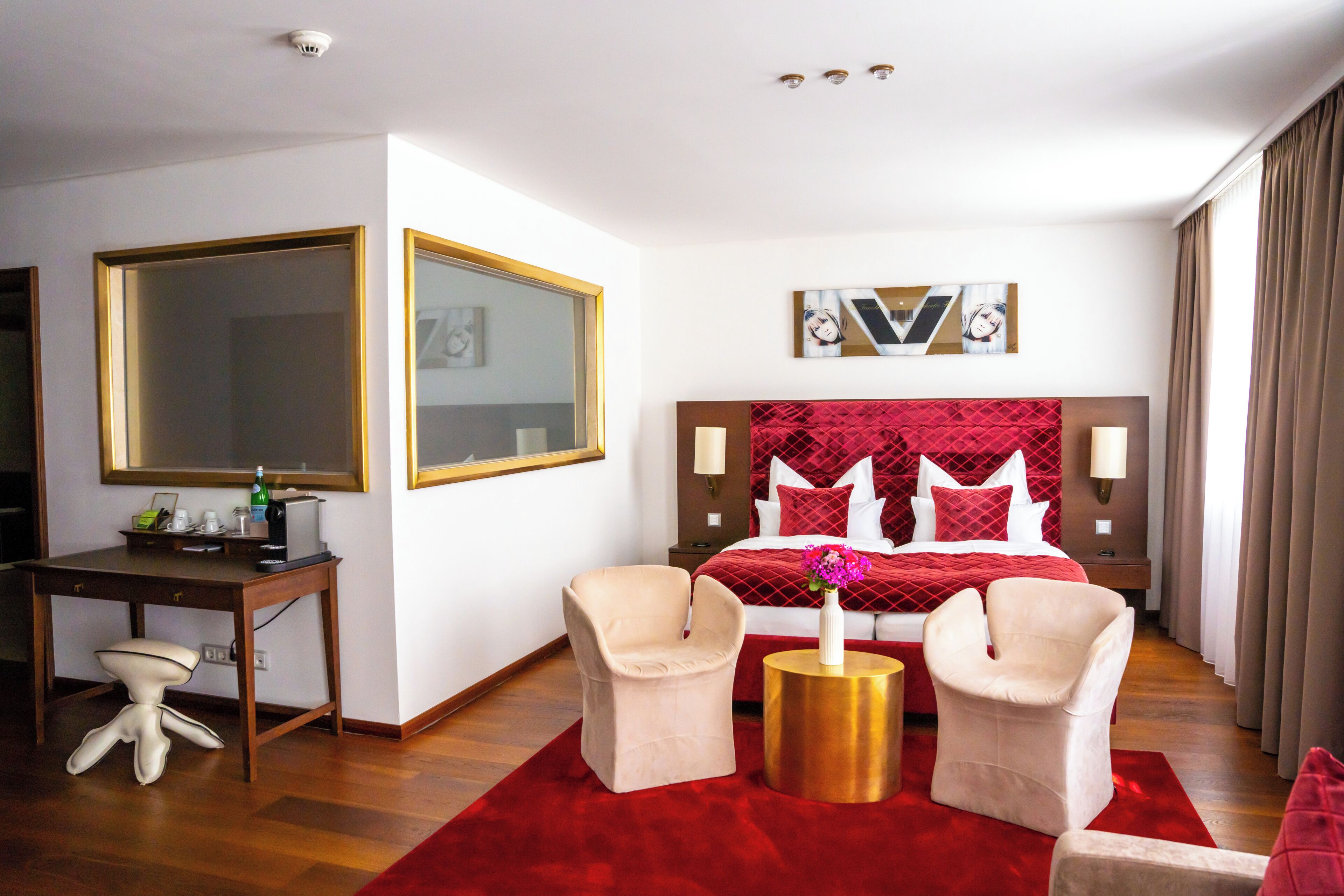 A hotel room with a large bed, two armchairs, a desk, and a mirror.